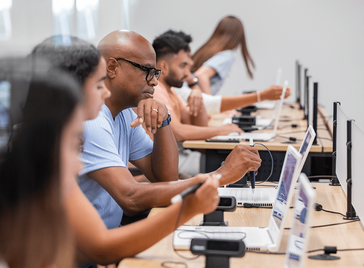 Row of Students at Desks Working at Laptops