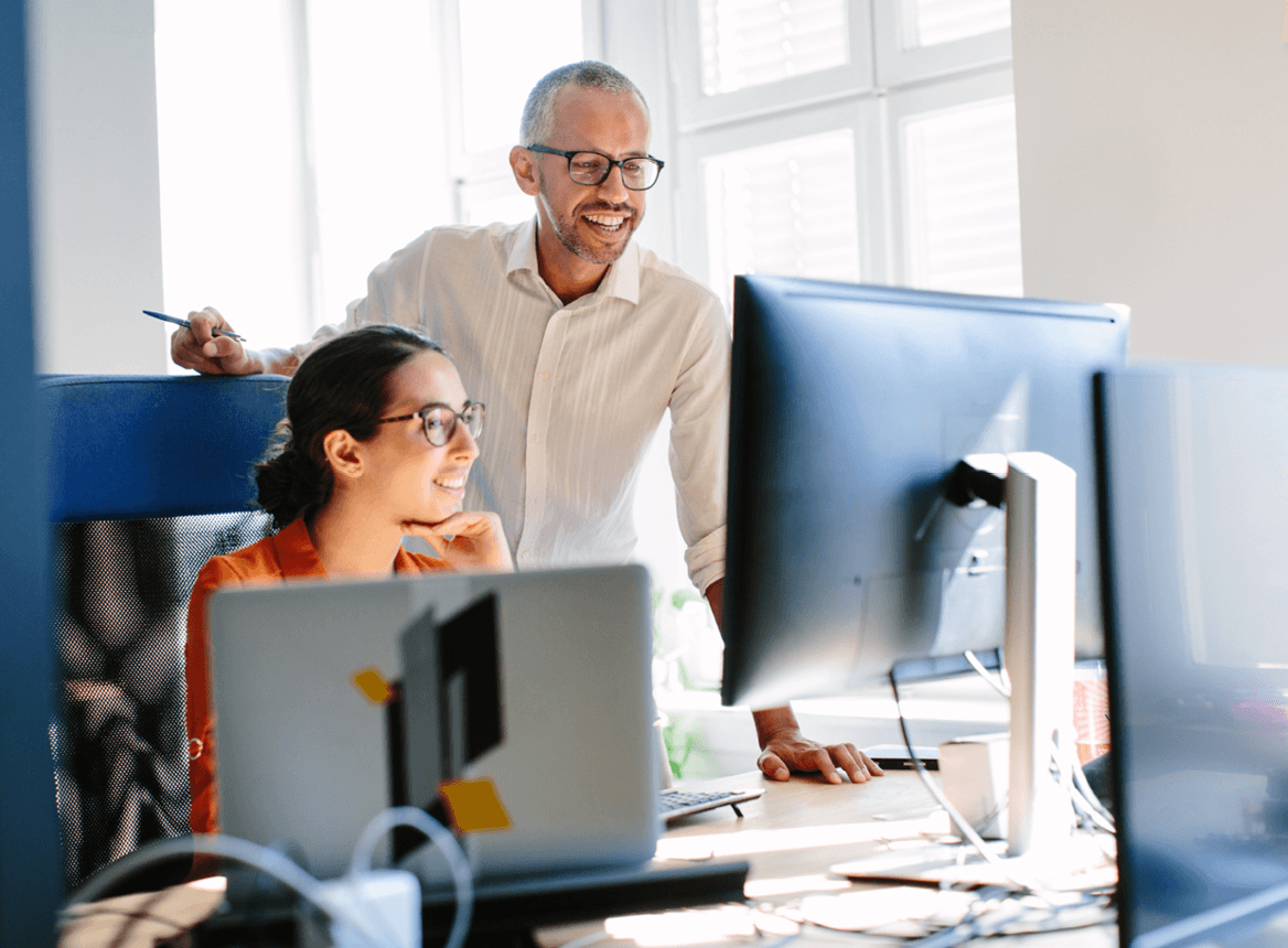 Two People in an Office Looking at a Computer and Smiling
