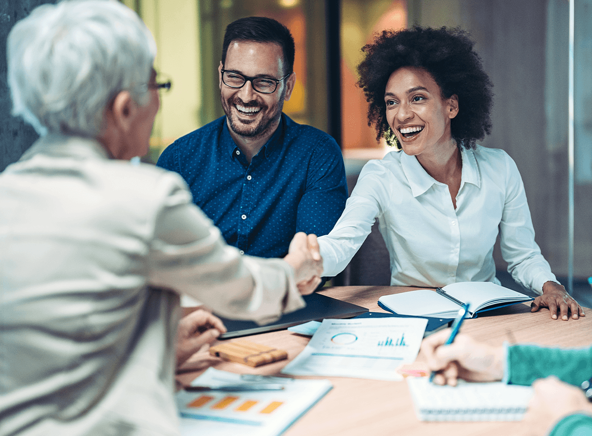 Three People Smiling in a Meeting and Shaking Hands Over a Table