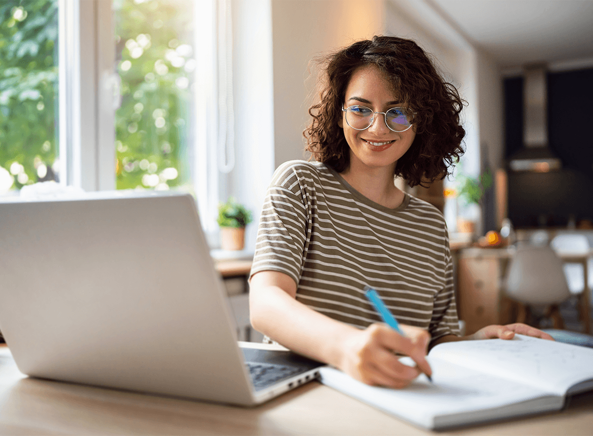 Woman with Glasses Working at desk on laptop holding pen Flag