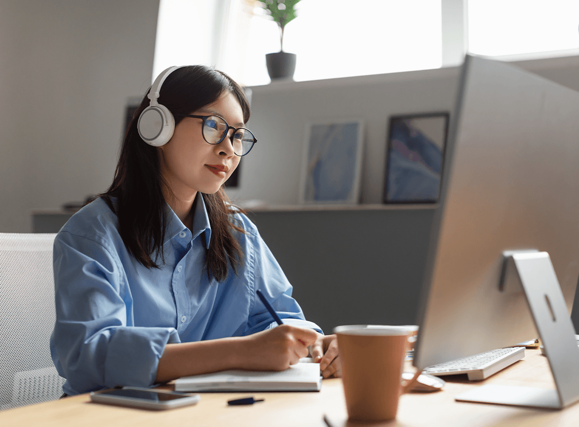 Woman studying from home writing on notepad with laptop with headphones on