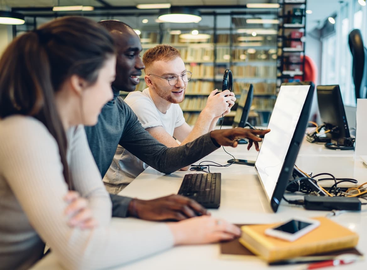 Three Students in a Library Looking at a Monitor